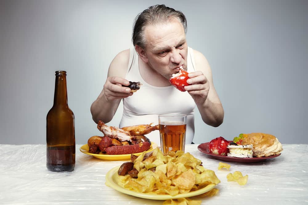 Aging man in a-shirt eating lot of junk food.