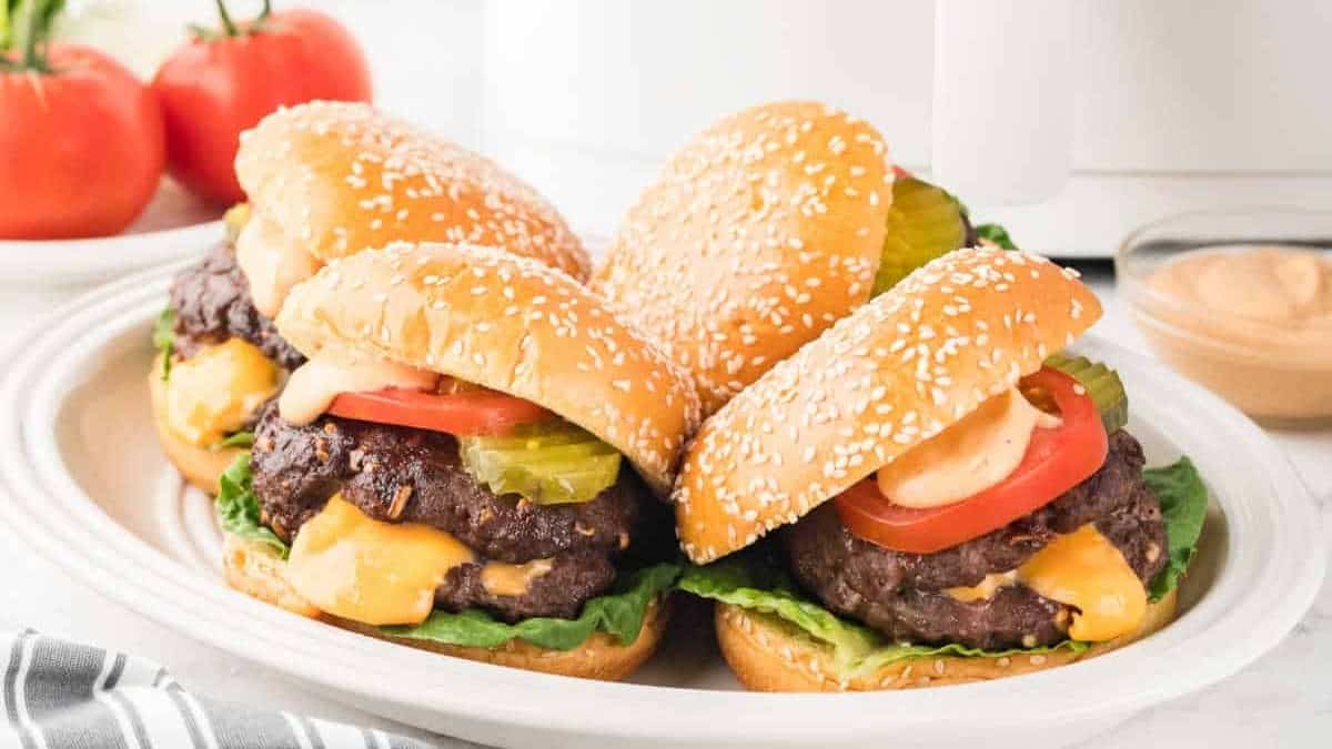 Four burgers on a plate with side dishes.