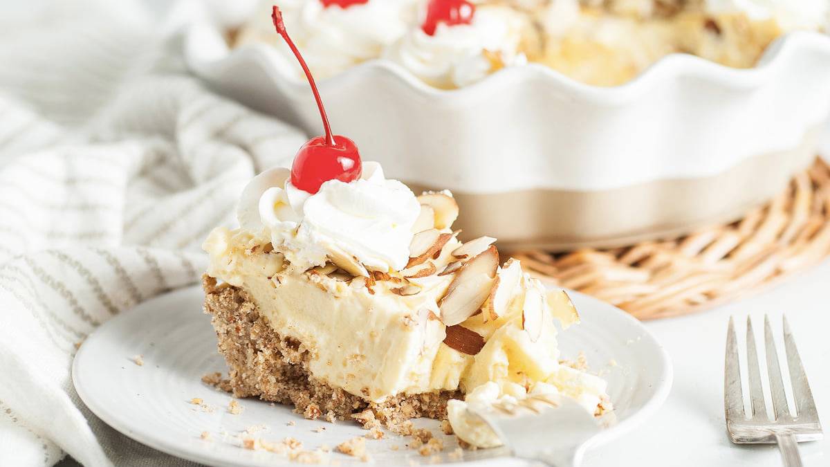 A delectable piece of amaretto pie adorned with a dollop of luscious whipped cream and crowned with a sweet cherry on top.