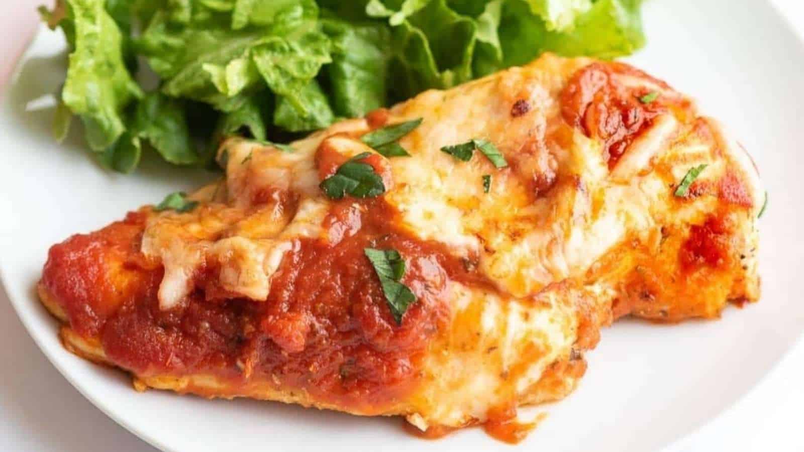 Chicken parmigiana on a white plate with a salad.