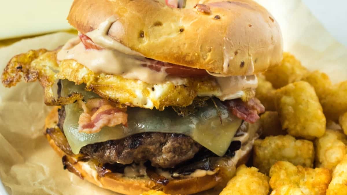 A burger topped with bacon and served alongside delicious tater tots.