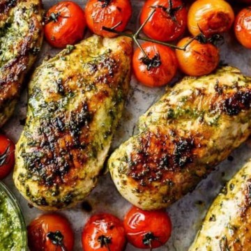 Chicken breasts with pesto and tomatoes on a baking sheet.