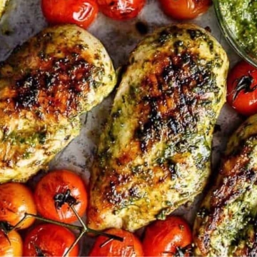 Chicken breasts with pesto and tomatoes on a shared baking sheet.