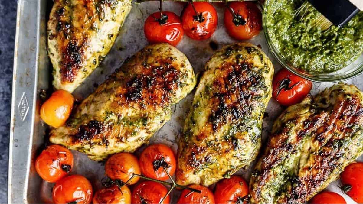 Chicken breasts with pesto and tomatoes on a shared baking sheet.