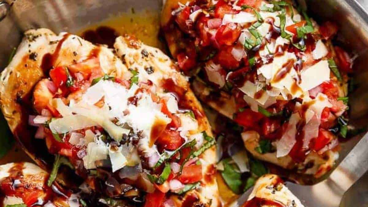 Chicken breasts topped with tomatoes and herbs in a pan.
