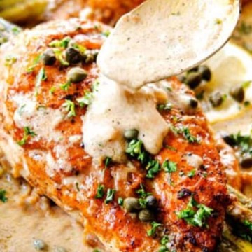 Chicken breasts in a skillet with lemon sauce and asparagus.