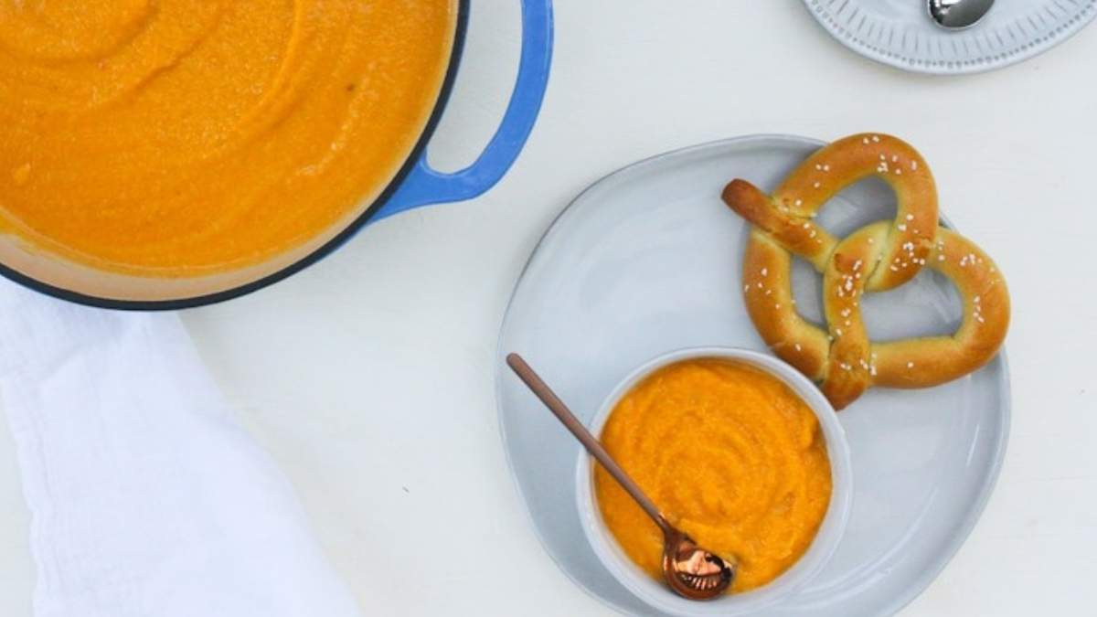 A delicious recipe for carrot soup served alongside warm, golden pretzels on a plate.