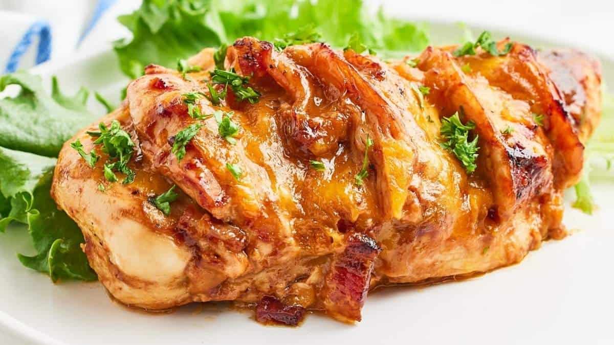 A chicken breast covered in cheese and bacon on a white plate.