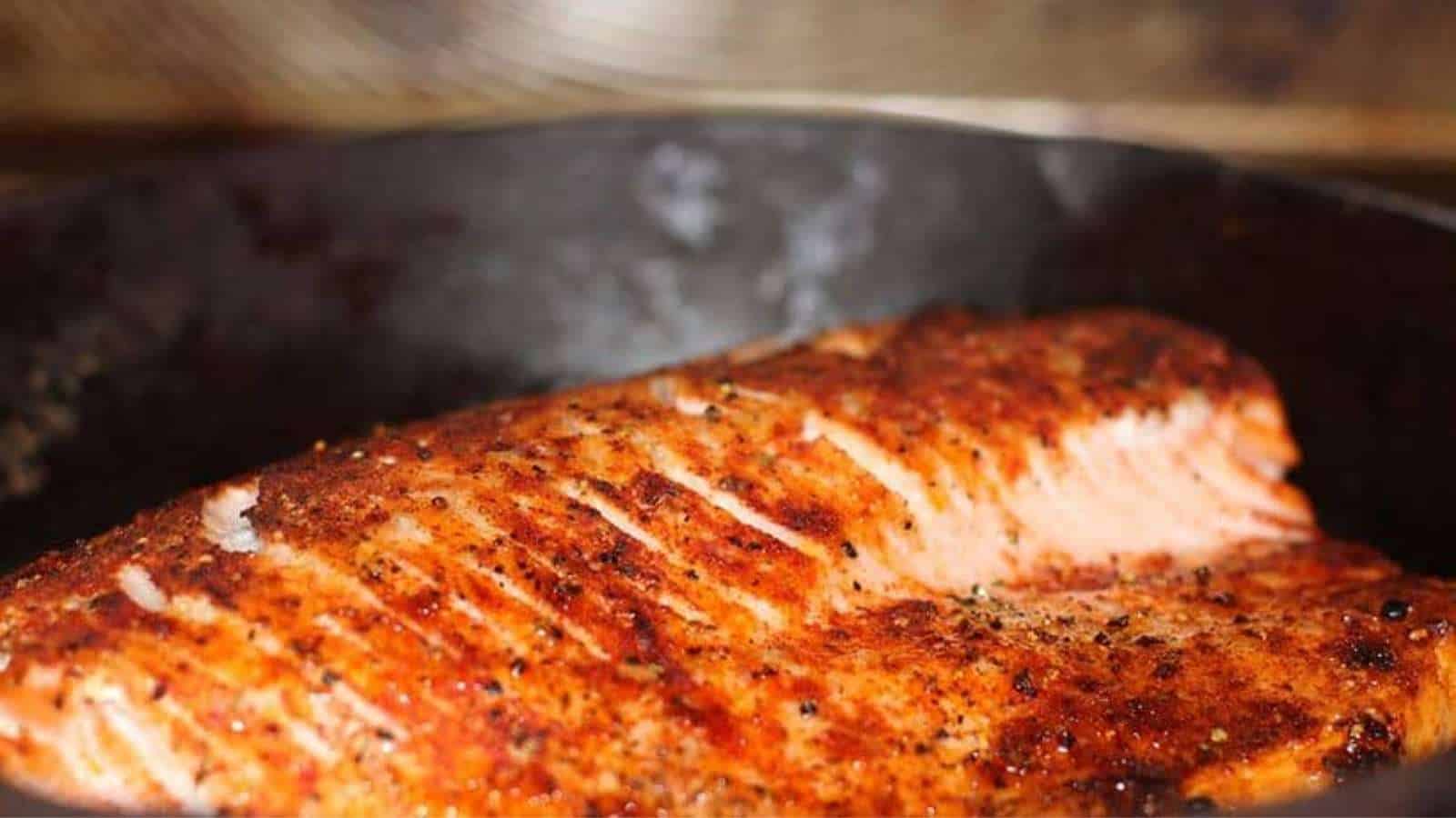 A piece of salmon is being cooked in a skillet.