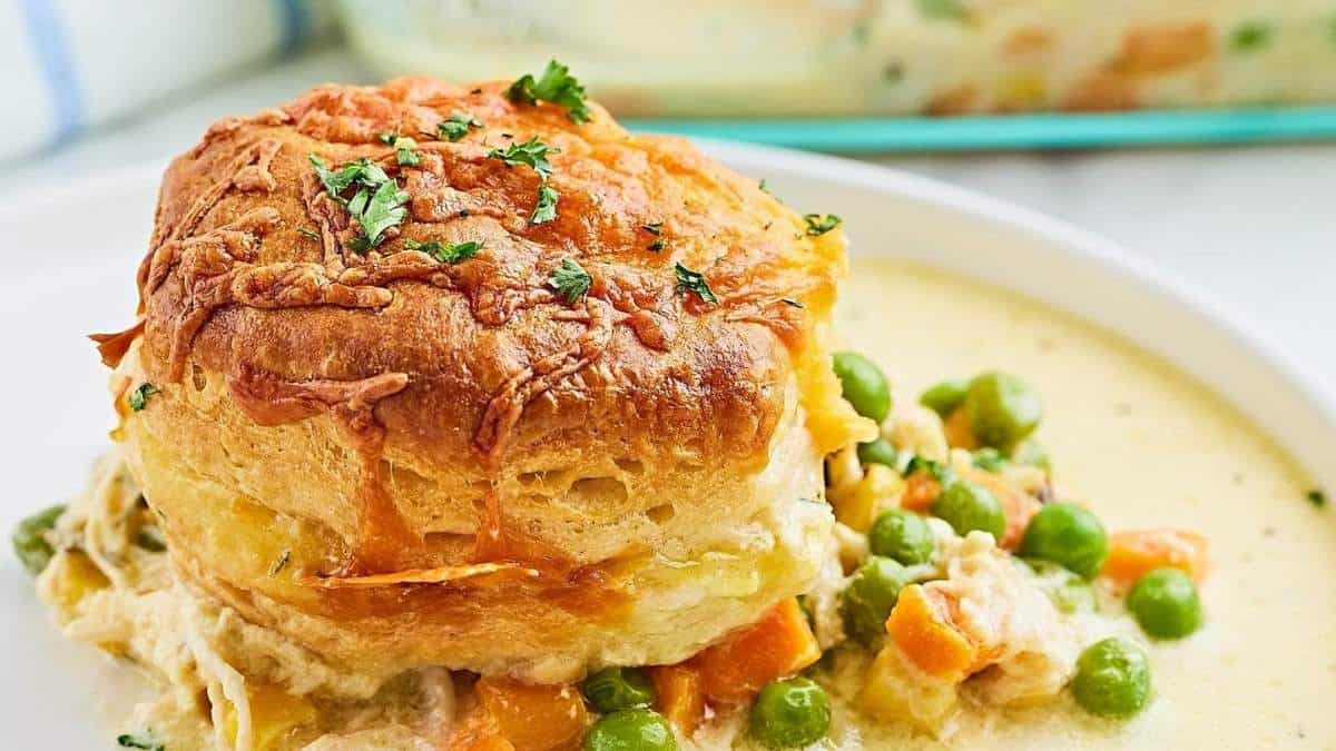 Chicken pot pie on a plate with peas and carrots.