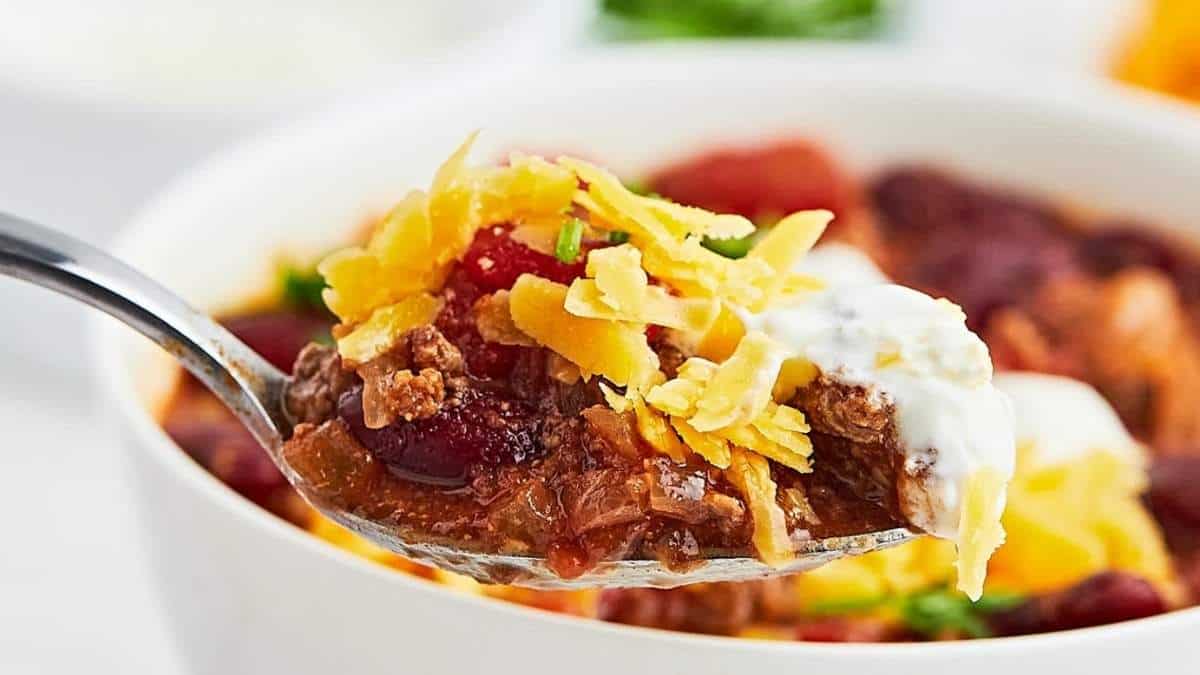 A spoon full of chili soup with cheese and sour cream.