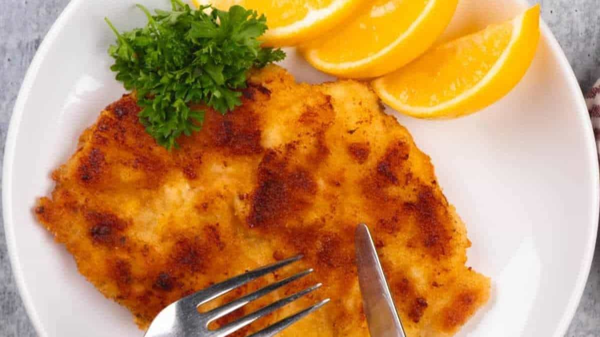 SHARED round up of Comfort Food Recipes - Chicken schnitzel on a plate with orange slices and a fork.