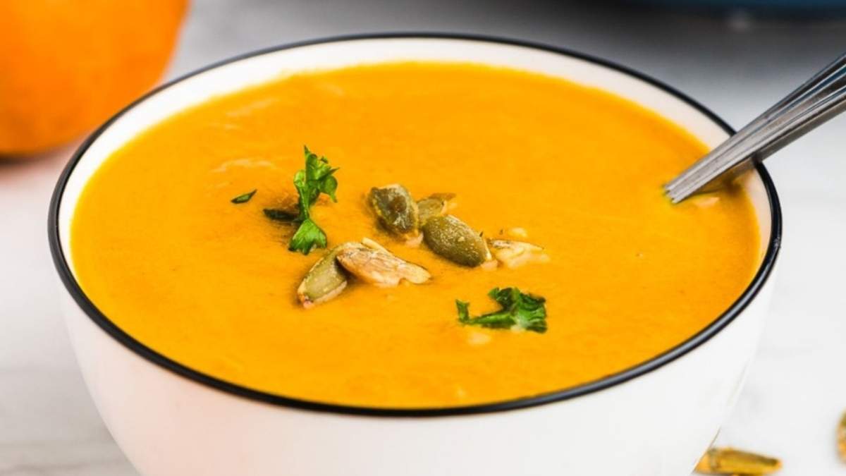 Delicious pumpkin soup served in a white bowl garnished with pumpkin seeds.
