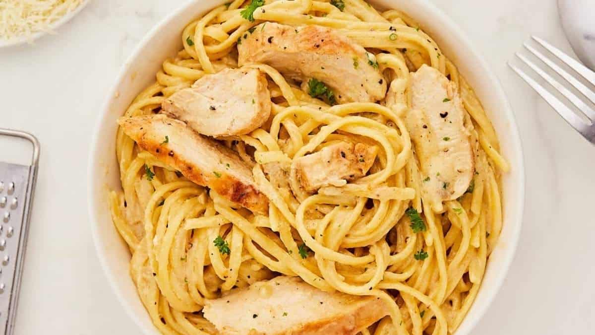 A white bowl of spaghetti with chicken and parmesan.