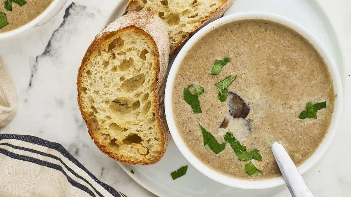 A delicious bowl of mushroom soup garnished with fresh parsley and served alongside warm, crusty bread. Perfect for a comforting meal on a chilly day.