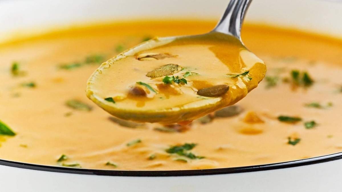 A spoonful of pumpkin soup in a white bowl, perfect for a comforting fall recipe.