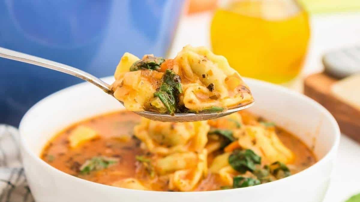 Delicious tortellini soup served in a bowl with a spoon.