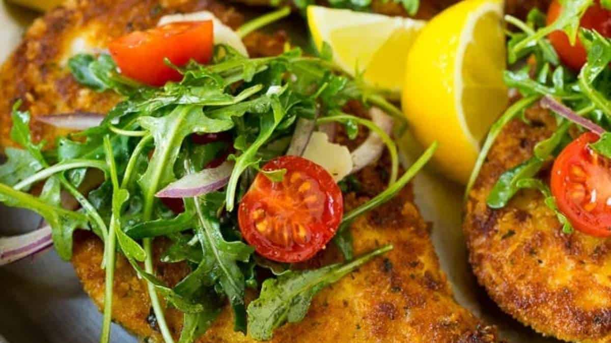 A plate with chicken breasts, tomatoes and arugula.