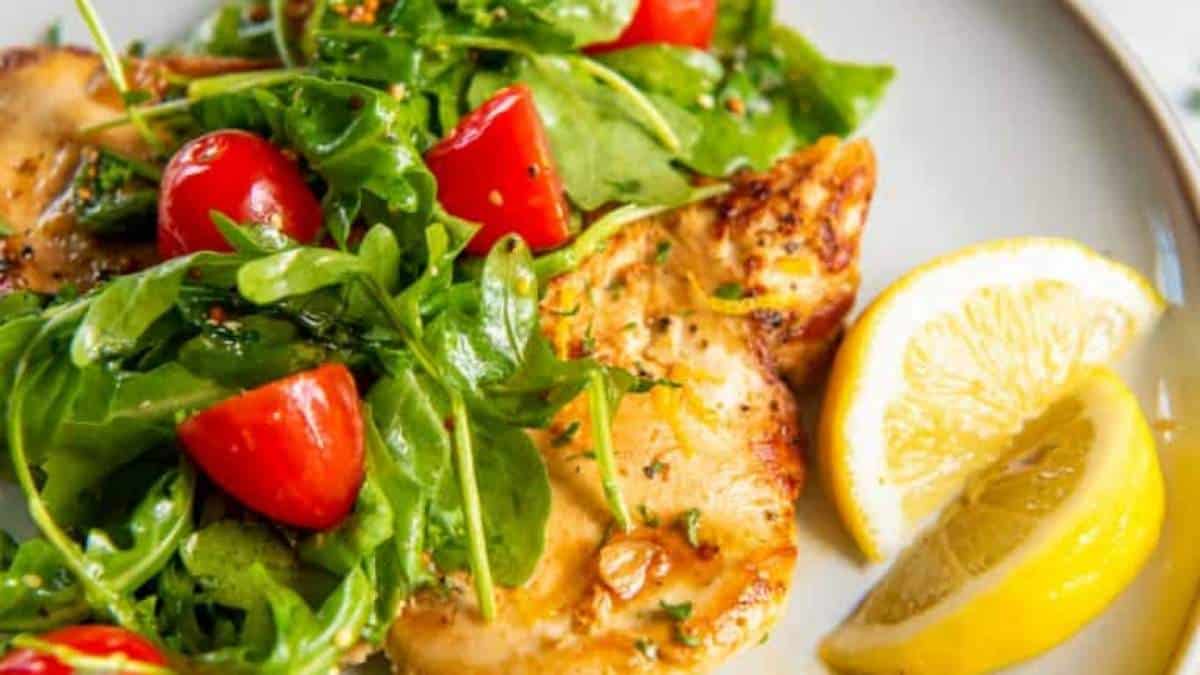 A plate of chicken with arugula and tomatoes.
