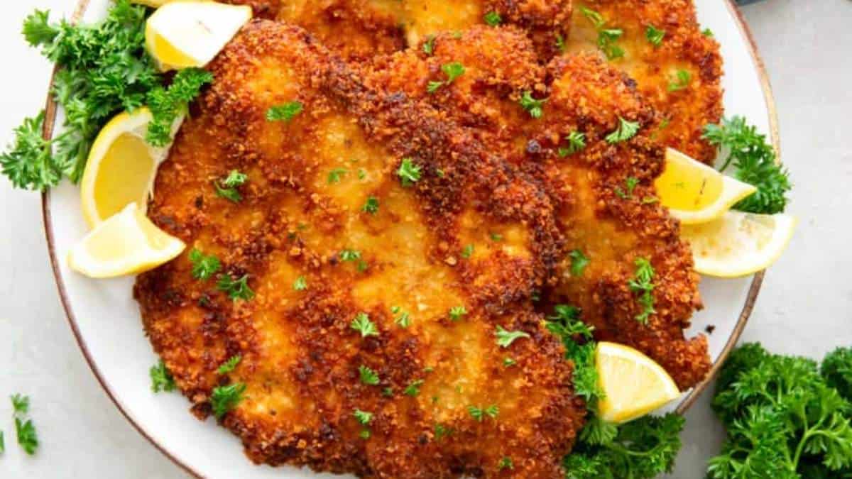 Fried schnitzel on a plate with lemon wedges.