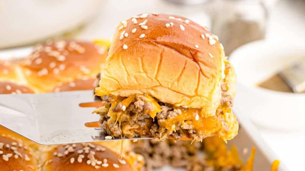 A fork is being used to take a piece of cheesy sliders, a popular side dish, out of a baking dish.