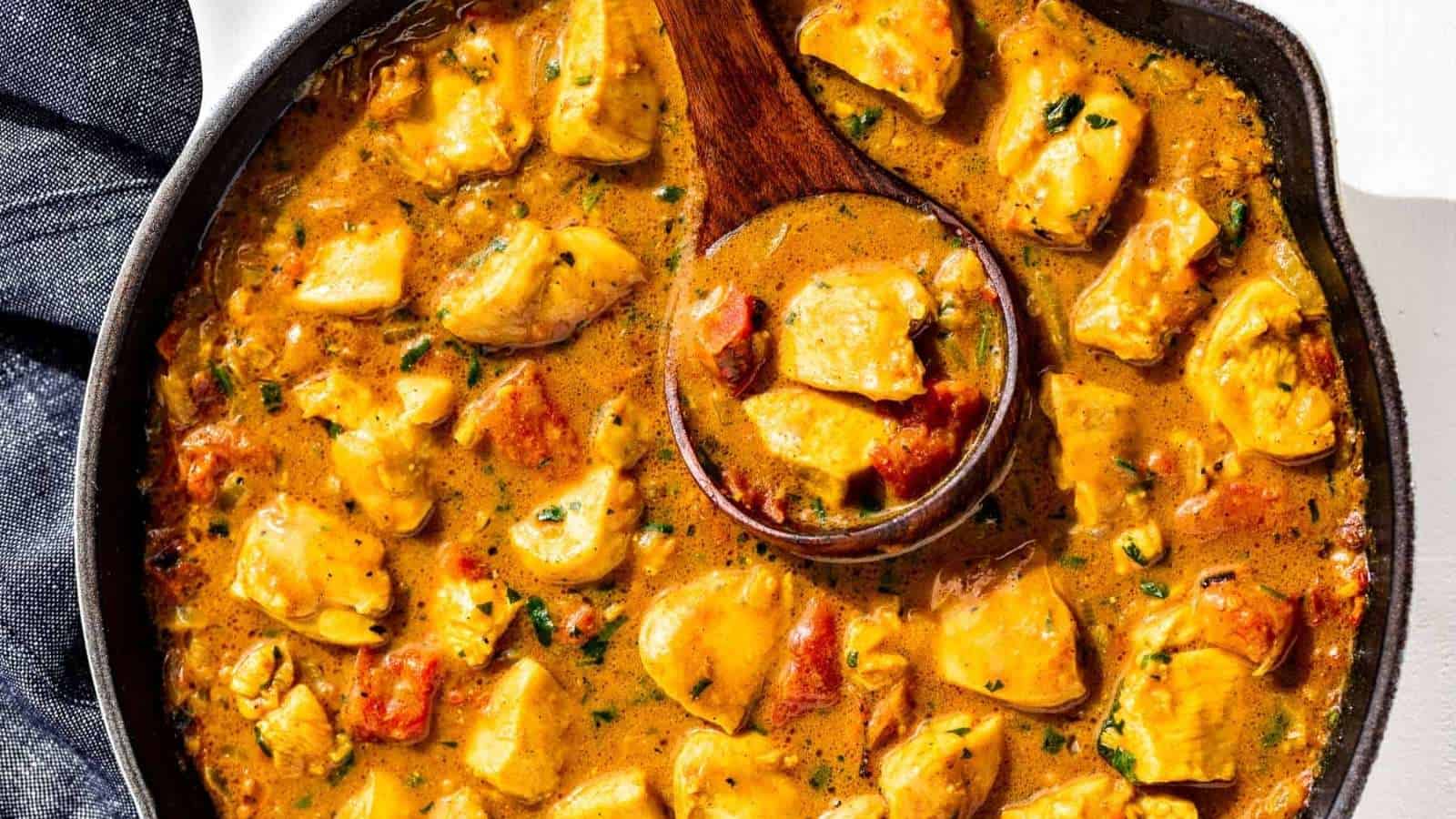 Chicken curry in a skillet with a wooden spoon.