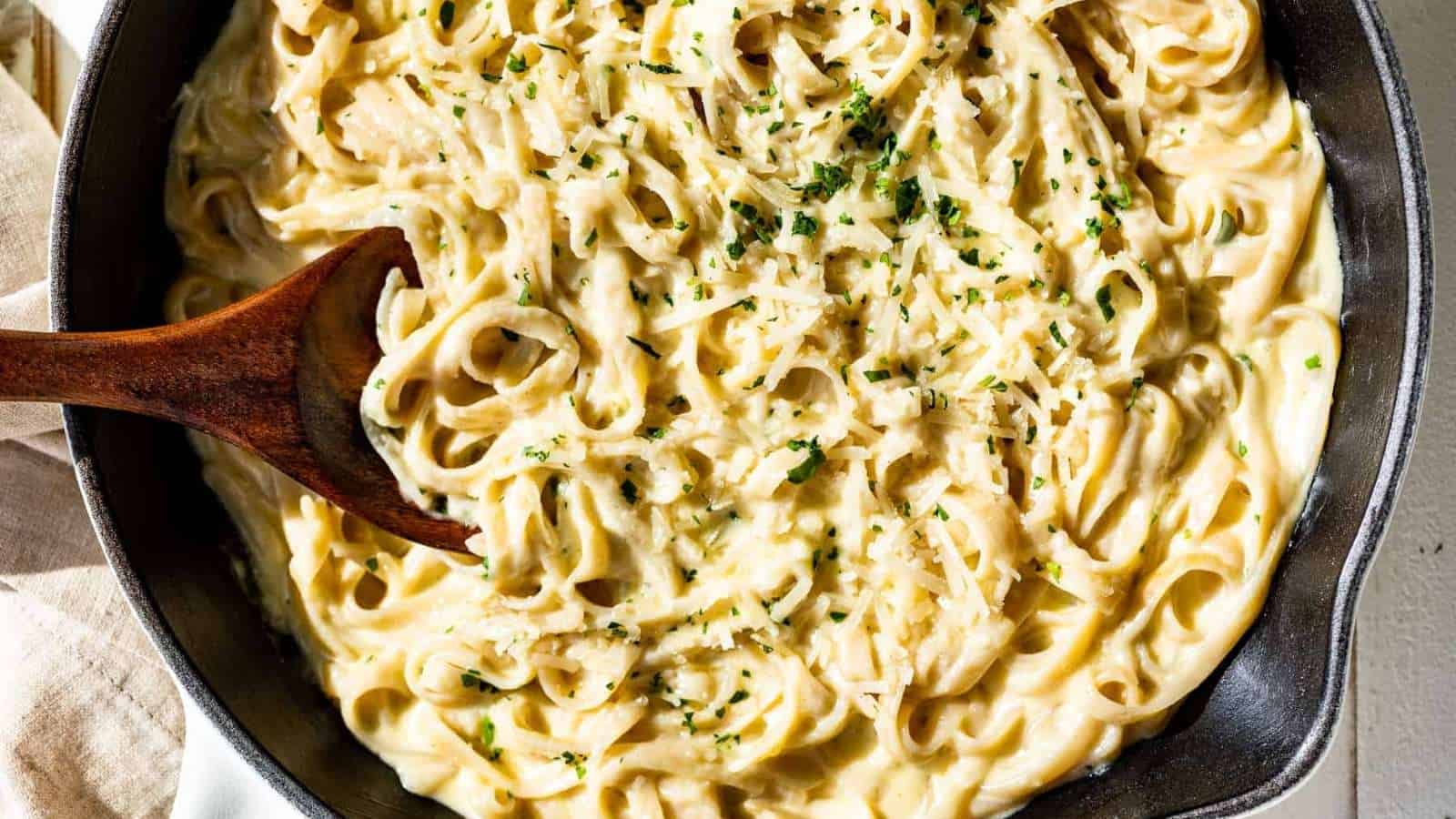 Cheesy pasta in a skillet with a wooden spoon.