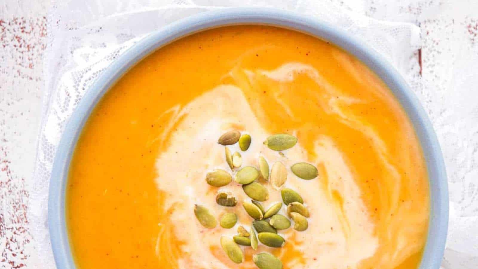 A bowl of pumpkin soup with pumpkin seeds on top.