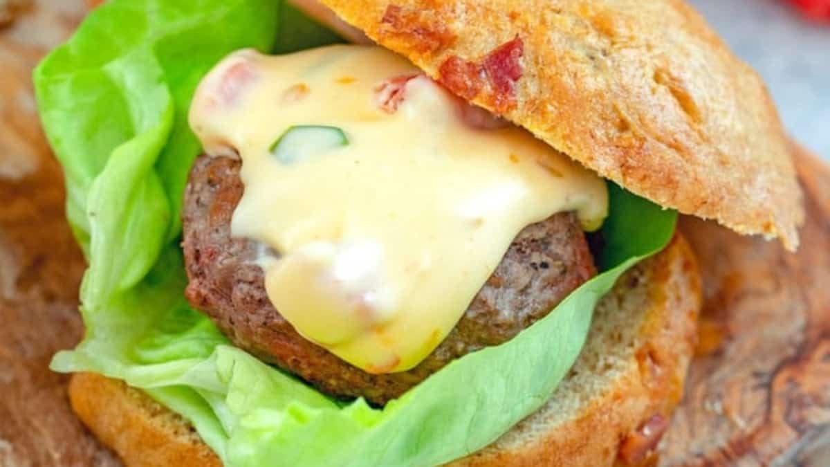 A burger with cheese and lettuce on a wooden cutting board, accompanied by a side of fries.
