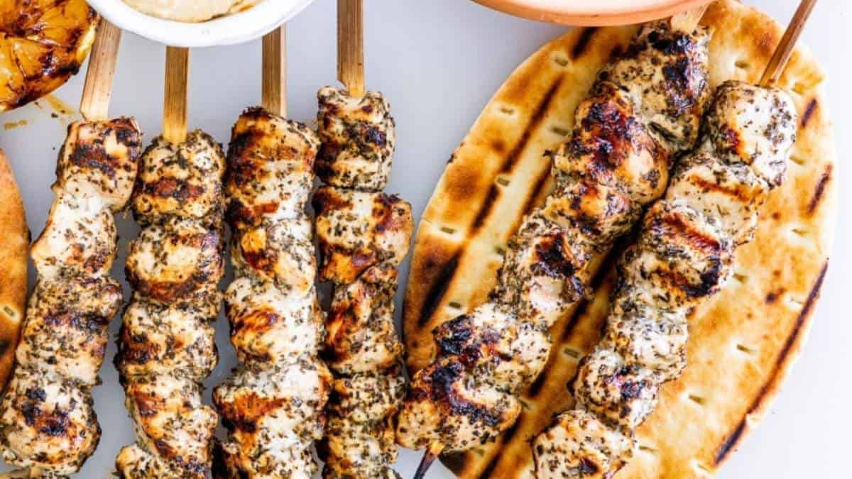 Grilled chicken skewers on skewers with dipping sauce.