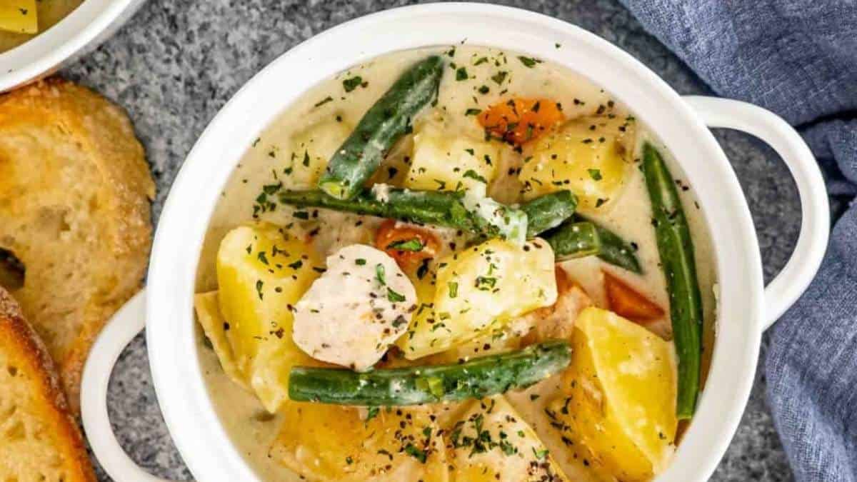 A white bowl with chicken, potatoes and green beans.