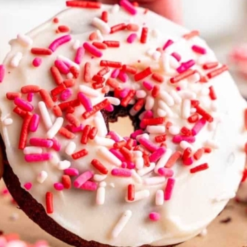 A person holding a Red Velvet donut with sprinkles on it.