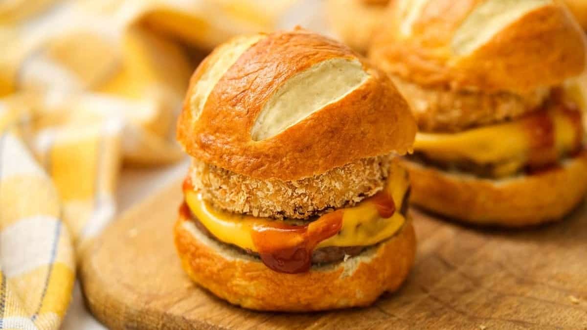 Burger sliders served with side dishes and displayed on a wooden cutting board.