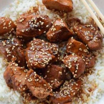 A white plate with sesame chicken, rice and chopsticks.