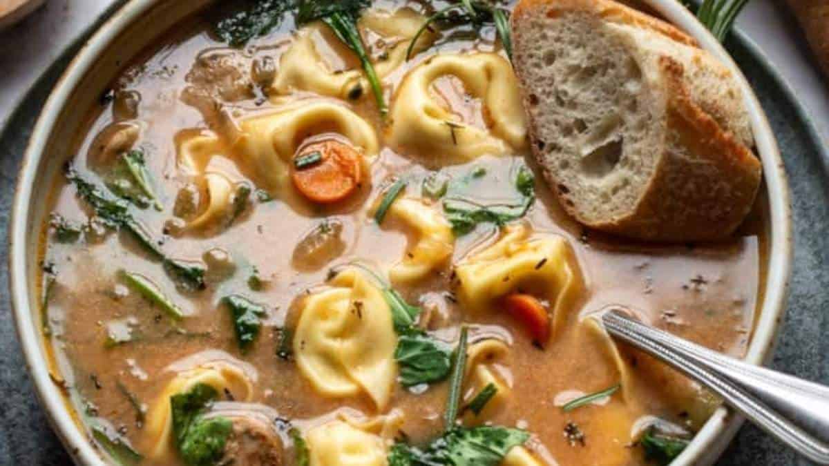 Keyword: soup recipe
Updated Description: A delicious bowl of tortellini soup, made with tender pasta filled with savory cheese, served alongside a slice of crusty bread and a sprinkle of nutritious spinach
