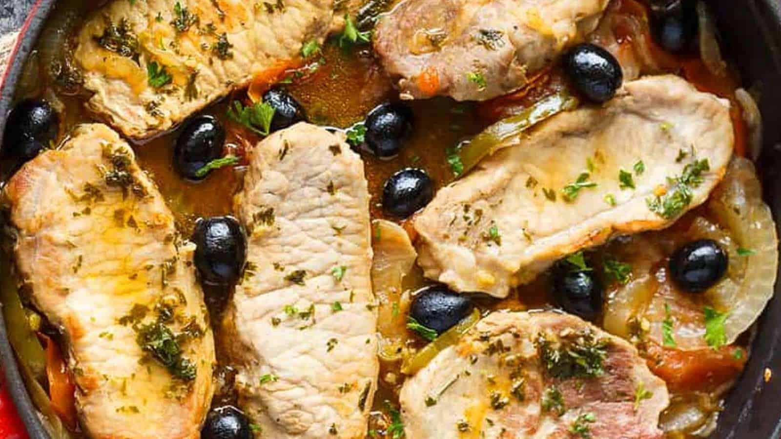 Pork chops with olives and tomatoes in a skillet.