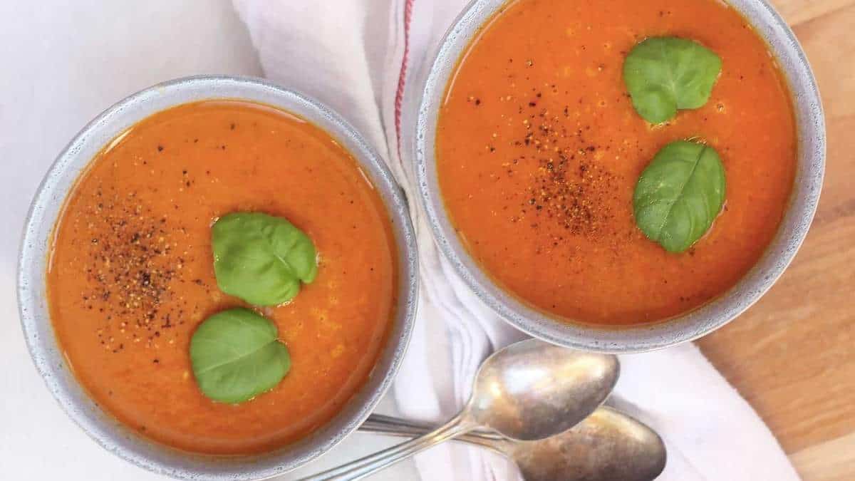 A savory recipe featuring two bowls of tomato soup garnished with fragrant basil leaves.