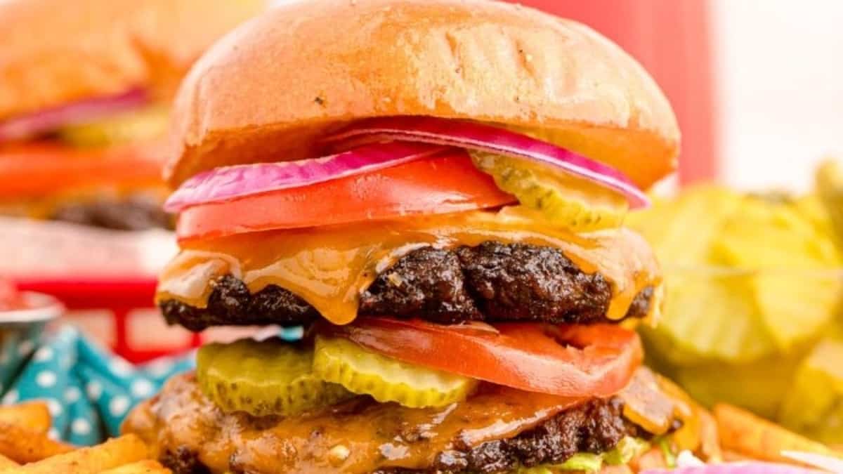 A stack of burgers and fries, along with side dishes, on a table.