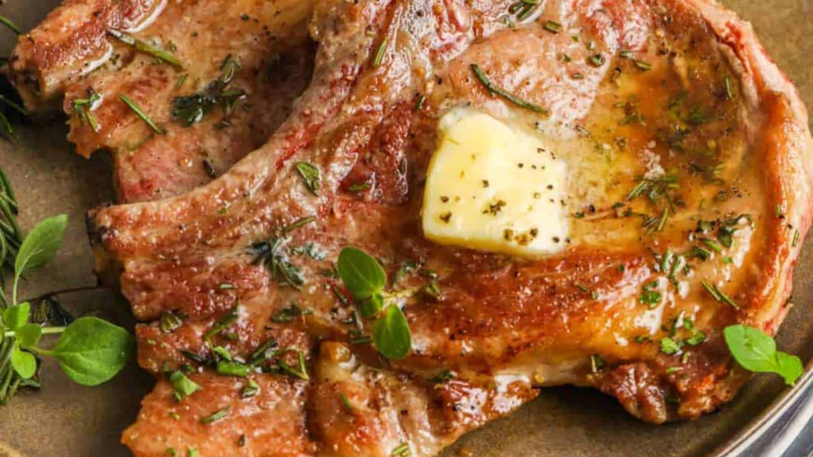 Pork chops on a plate with butter and sprigs of thyme.