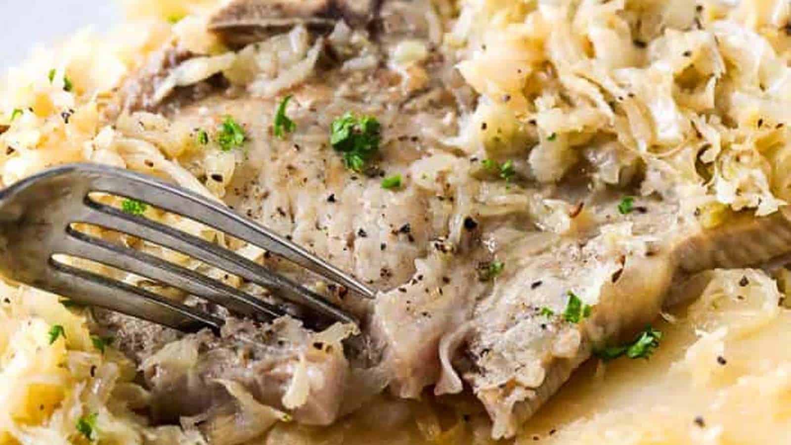 A fork is taken out of a plate of sauerkraut and meat.