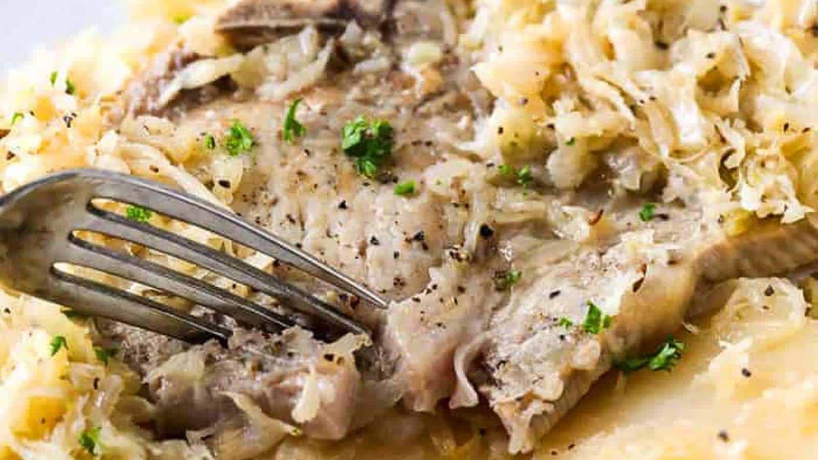 A fork is taken out of a plate of sauerkraut and meat.