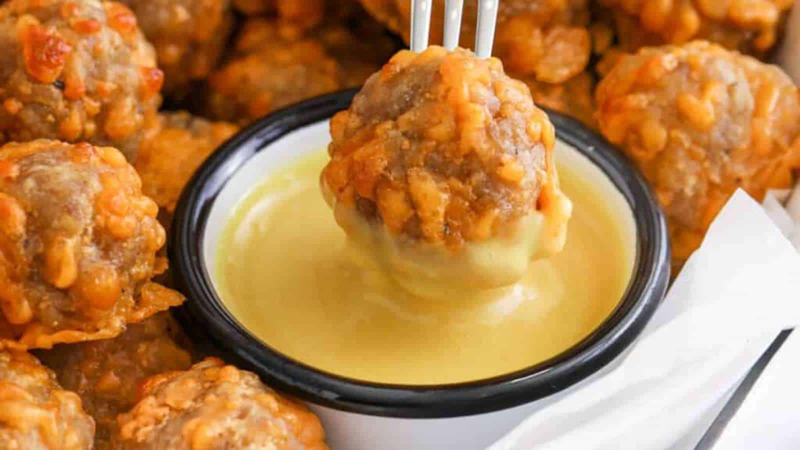 Cheesy meatballs being dipped in a sauce.
