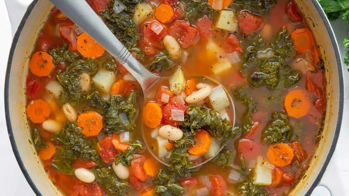 A delicious pot of kale and white bean soup with a spoon.