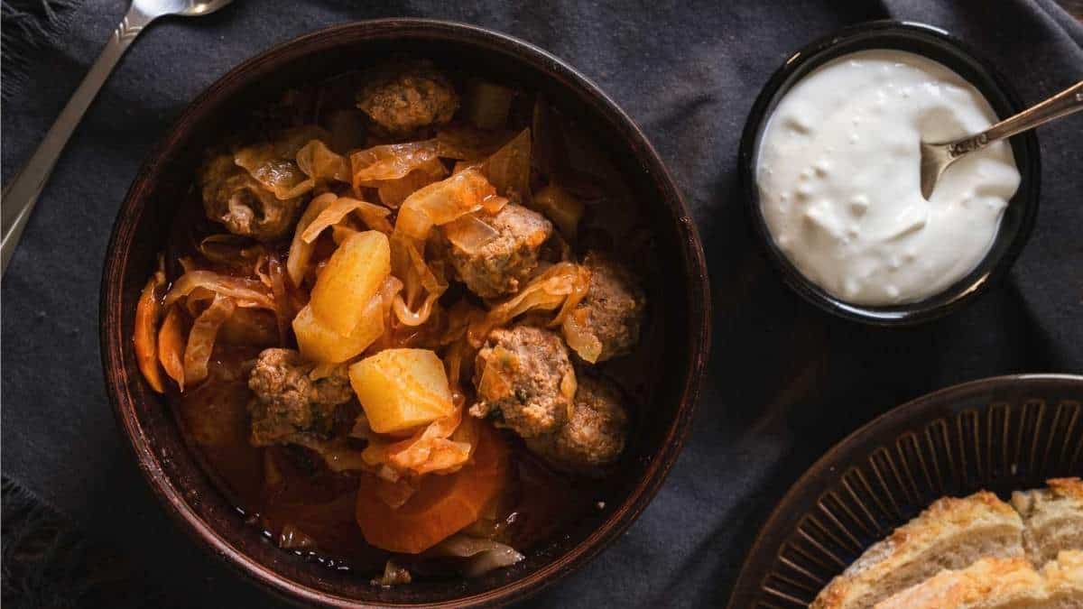 A bowl of meatball stew with bread and sour cream, perfect for soup lovers craving a hearty meal.