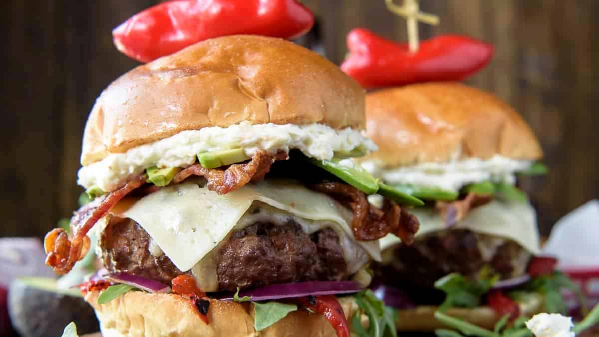 Two burger sliders served on a wooden board with side dishes.