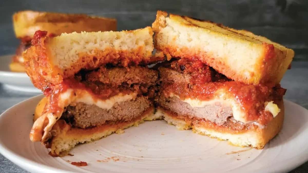 A Ham sandwich with meat and sauce on a plate, served with side dishes.
