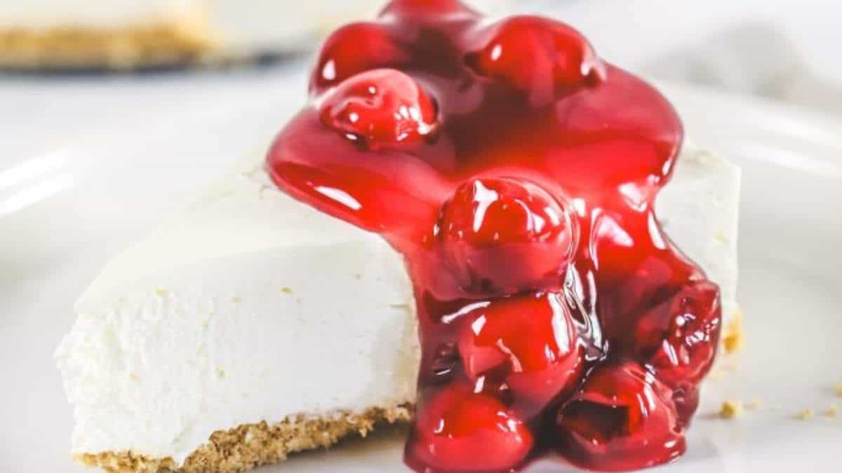 A slice of cherry cheesecake, a shared indulgence with its round shape elegantly presented on a white plate.