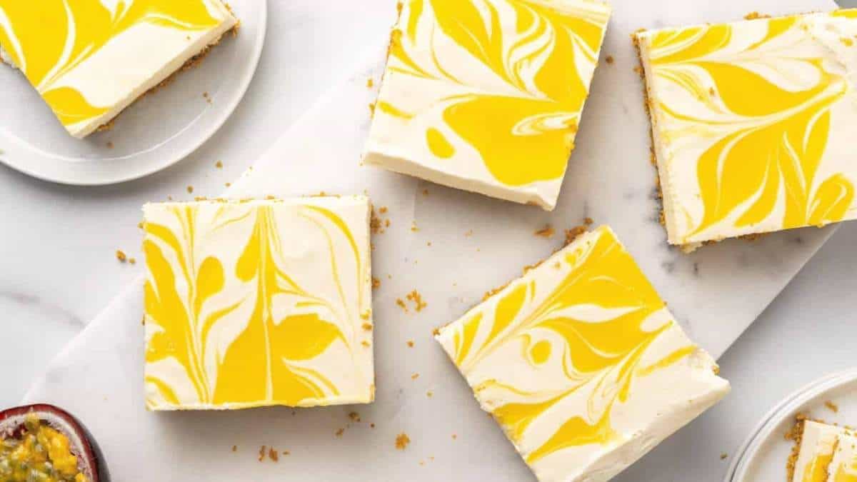 Four squares of yellow and white marbled cheesecake on a white plate, perfect for a shared indulgence or as part of a round-up of delectable no bake desserts.