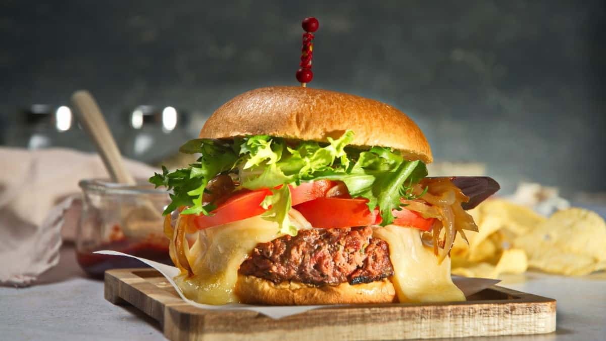A mouthwatering burger on a wooden cutting board, served with delicious side dishes.