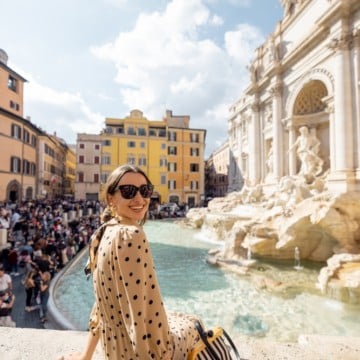 A woman is enjoying a relaxing weekend getaway, sitting on the edge of the Trevi Fountain in Rome.